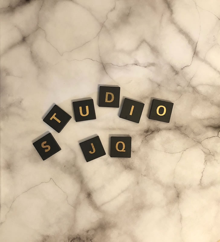 A marble table top displaying several black scrabble pieces which spell out the word "Studio JQ" in gold lettering