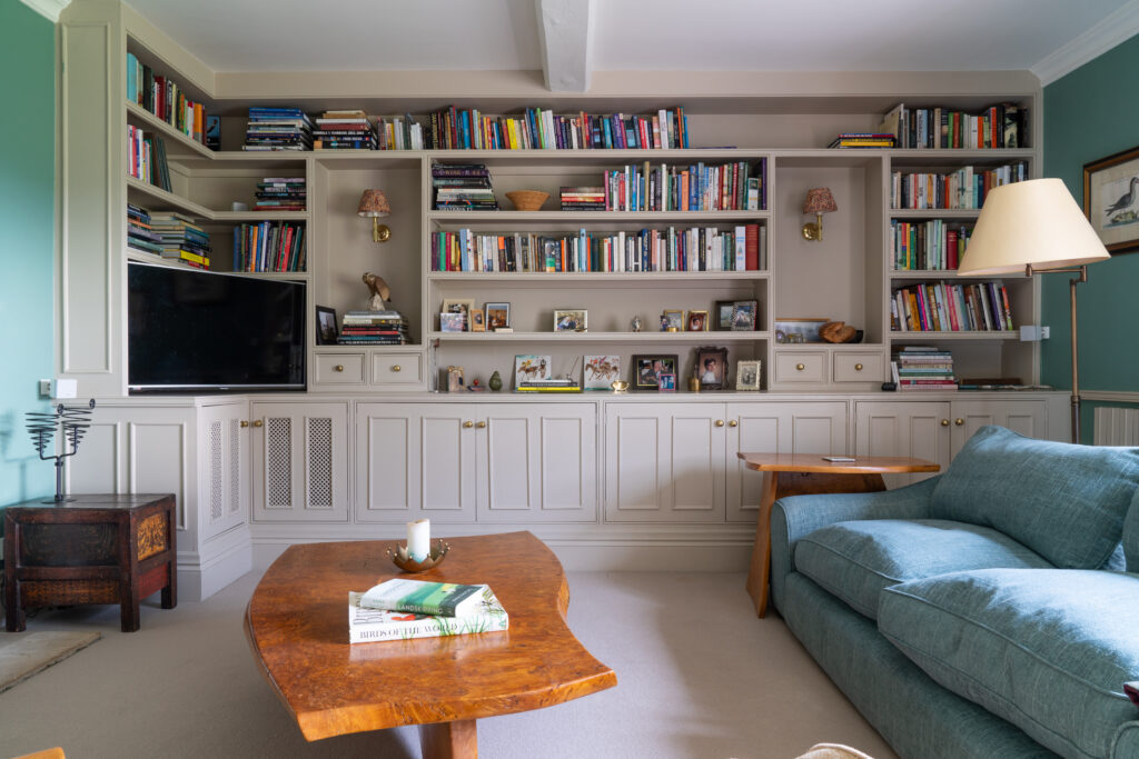 A beautiful room, displaying a large bookcase, bespoke wooden table centrepiece and comfortable blue sofa, showcasing Studio JQ's interior design services